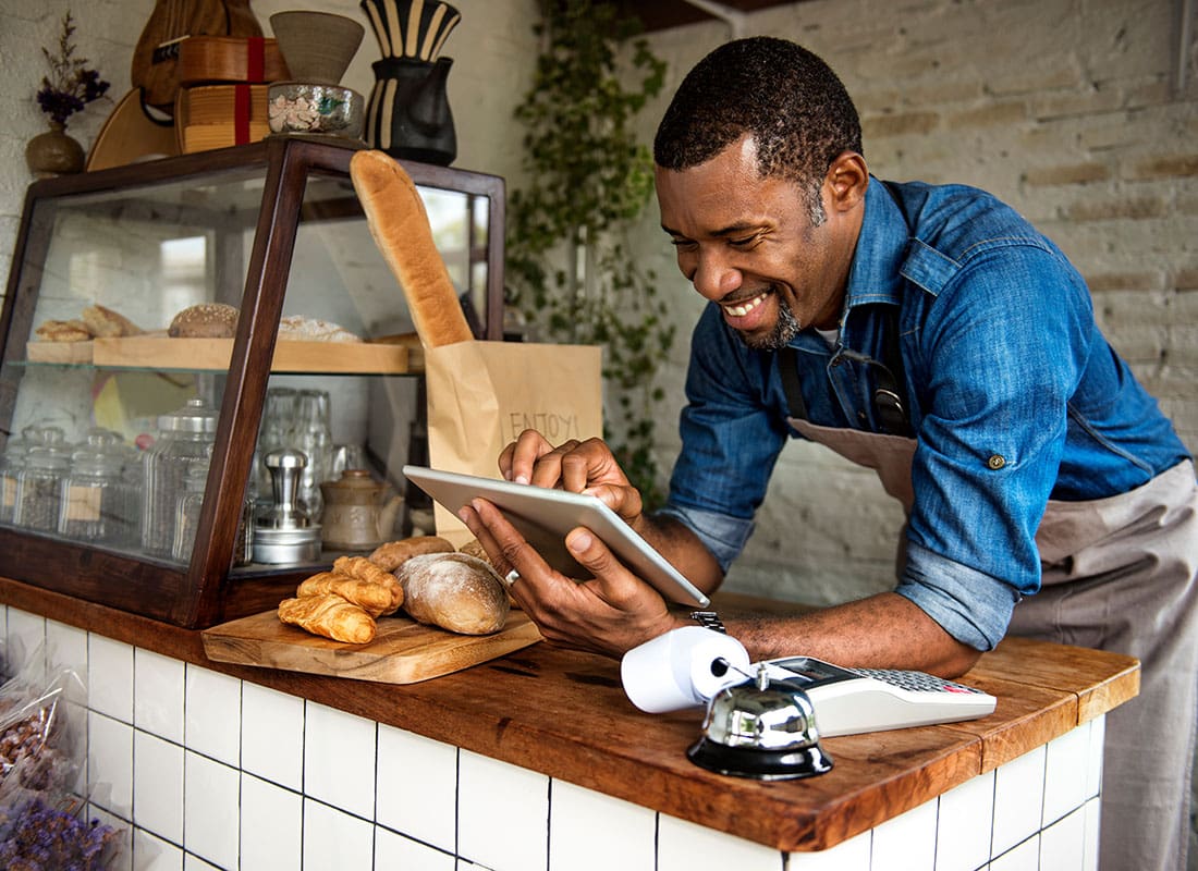 Business Insurance - Portrait of a Smiling Young Business Owner Standing in his Bakery Behind the Front Counter While Using a Tablet